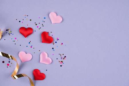 Valentine's day festive background. Pink and red hearts with multicolored confetti around on purple...