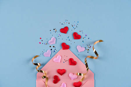 Valentine's day festive background. Pink envelope with red hearts confetti around on pastel blue background with copy space. Flat lay, top view. Greeting cardの写真素材
