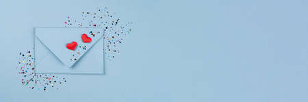 Banner. Valentine's day festive background. Blue envelope with red hearts and multicolored confetti around on pastel blue background with copy space. Flat lay, top view. Greeting card, invitationの写真素材