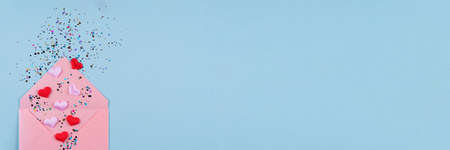 Valentine's day festive banner background. Pink envelope with red hearts confetti around on pastel blue background with copy space. Flat lay, top view. Greeting cardの写真素材