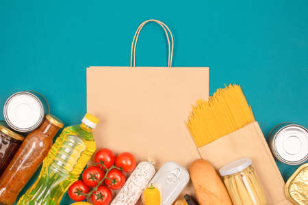 Food bank, food delivery concept. Paper bag with food donations on green background with copy space - pasta, fresh vegatables, canned food, baguette and other groceries. Mockupの写真素材