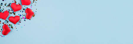 Valentine's day festive banner background. Red hearts with multicolored confetti around on trendy pastel blue background with copy space. Flat lay, top view. Greeting card, invitationの写真素材