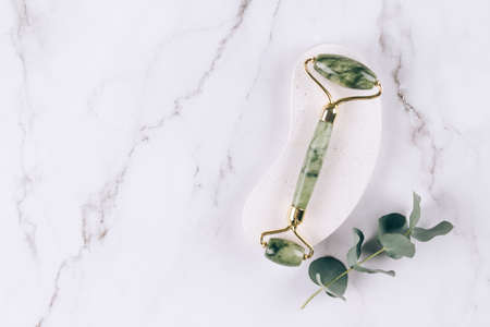 Close up view of jade facial roller gua sha on white marble table background. Facial massage kit for lifting massage therapy made from natural stones, personal skin care anti-aging toolsの写真素材