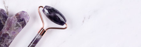 Banner with facial massage kit - amethyst gua sha tool and face roller on white marble background. Face roller, massager made from natural stones, home spaの写真素材