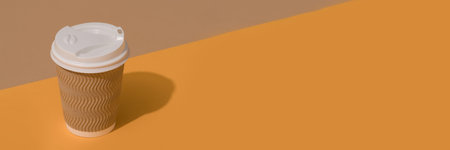 Banner with brown eco coffee cup with white plastic lid on orange and brown background with copy spaceの写真素材