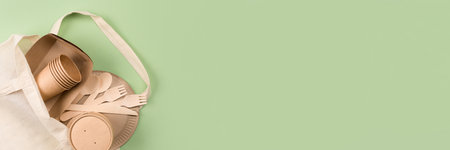 Banner with eco-friendly paper tableware - kraft paper food cups and containers in cotton bag on light green background with copy space. Street food take away paper utensilsの写真素材