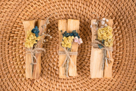 Top view on palo santo sticks with bouquets of dried flowers on natural straw background. Holy wood...