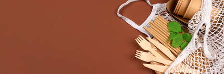 Banner with kraft paper food cups and containers with wooden cutlery in white cotton net bag on brown background with copy space - eco-friendly tableware. Street food take away paper packaging. Selective focusの写真素材