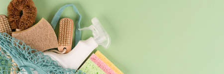 Banner with green household products on green background with copy space. Bamboo brush, organic dishcloth, lemon, baking soda, citric acid, cleaning liquid in spray bottle in cotton net bagの写真素材
