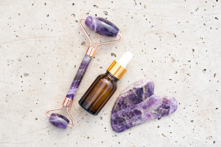 Flat lay composition with facial massage kit - amethyst gua sha tool and face roller with beauty...