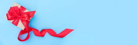 Festive Christmas banner with present box with red ribbon bow on light blue background. Gift box with sparkles. Festive background with copy space for your projectの写真素材