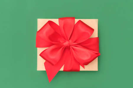 Present box with red ribbon bow on green background. Birthday or Christmas gift concept. Flat lay compositionの写真素材