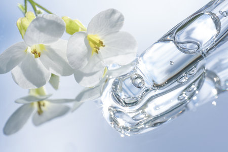 Pipette with transparent liquid with white flowers around on blue mirror background. Texture of face serum or cosmetic oil. Selective focus, beauty cosmeticsの写真素材