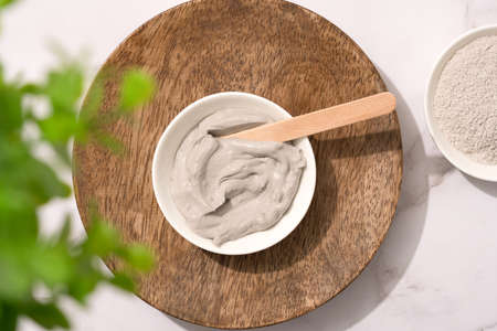 Bowl with gray cosmetic clay cream on wooden tray - mineral bentonite facial mask. Skincare beauty concept. Top viewの写真素材