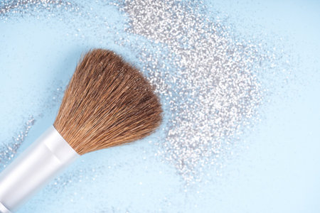 Festive holiday or Christmas makeup concept. Makeup brush over pastel blue background with silver sparkles and glitter around. Template with copy space for textの写真素材