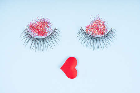 Festive holiday makeup. Eyelashes with red glitter eyeshadows and rep lips over pastel blue background. Creative make up and beauty conceptの写真素材