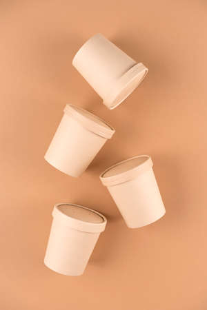 Eco kraft paper food containers for soup or hot beverages and food take away, cups with paper cap over light brown background, mockup image. Sustainable food packaging concept. Vertical imageの写真素材