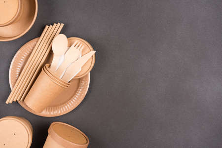 Set of eco paper tableware and utensils - paper cups, plates, containers and wooden bamboo cutlery over dark gray concrete background with copy space. Sustainable food packaging conceptの写真素材