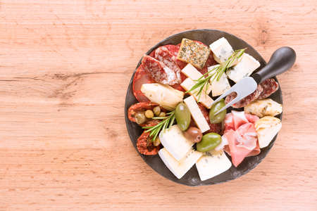 Italian antipasti plate with variety of cheeses, sausages served with sun dried tomatoes, olives and herbs on wooden table - parmesan, dorblu, prosciutto, salami. Cheese and meat snacks platter.  Menu background with copy spaceの写真素材