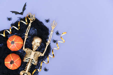 Funny and creepy halloween composition with black cobweb, spiders, pumpkins, bats and golden skeleton over purple with copy space for text. Party invitation templateの写真素材