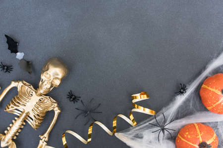 Festive halloween composition with white cobweb, spiders, pumpkins, bats and golden skeleton over gray concrete background with copy space for text. Party invitation templateの写真素材