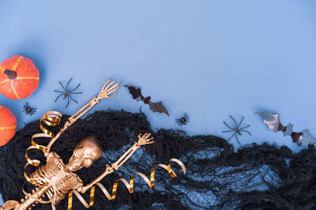 Funny halloween composition with black cobweb, spiders, pumpkins, bats and golden skeleton over blue with copy space for text. Party invitation templateの写真素材
