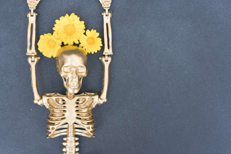 Funny halloween composition with golden skeleton wearing wreath of flowers over gray concrete background with copy space for text. Party invitation card templateの写真素材