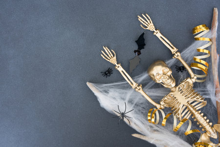 Creepy and funny halloween composition with white cobweb, spiders, bats and golden skeleton over gray concrete background with copy space for text. Party invitation card templateの写真素材