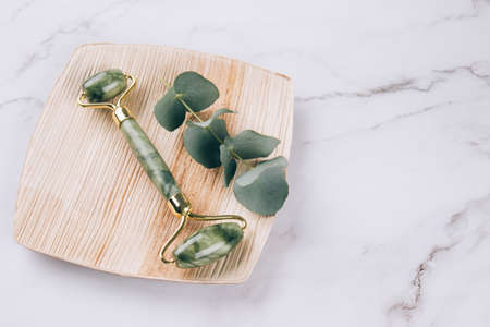 Face massage bundle. Jade facial roller gua sha over white marble table background. Facial massage tool for lifting therapy made from natural stones. Skin care tools. Selective focusの写真素材