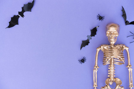 Trendy Halloween background with golden skeleton, bats and spiders over purple background with copy...
