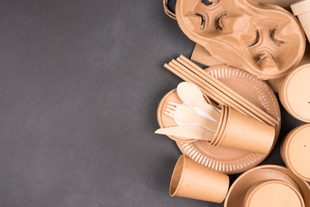 Paper utensils over dark concrete background with copy space - paper cups, food containers, bags and...