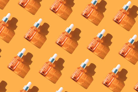 Pattern made of glass bottles with face serum or beauty oil with vitamin C over orange background. Beauty skin-care products with natural ingredients and fruit essence. Mockup, open compositionの写真素材