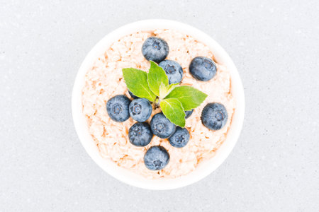 Healthy breakfast - oatmeal porridge served with blueberry and mint leaves on concrete table...