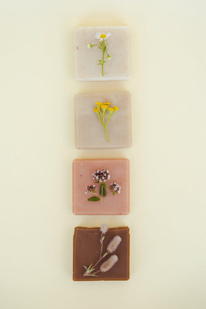 Soap bars made with natural herbal essential oils, flowers and herbs over light yellow background....