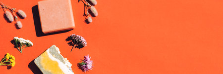 Banner with handmade herbal organic soap bars made with natural ingredients, flowers and herbs over orange background with copy space. Top view, flat lay styleの写真素材
