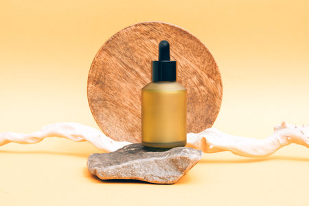 Matte glass dropper bottle with organic cosmetic oil or face serum against light yellow background with stone and wooden stick as decorations. Natural skin care products. Mockupの写真素材