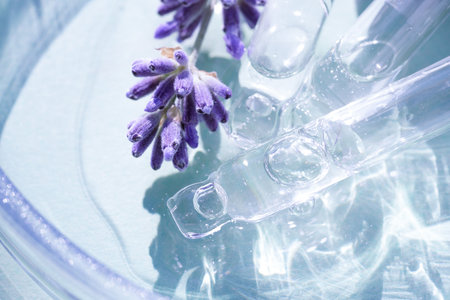 Pipette with cosmetic liquid or face serum with lavender flowers over blue background. Texture of hydrolate or cosmetic oil with lavender extract for skin care. Selective focusの写真素材