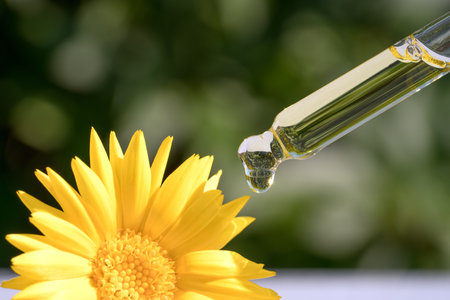 Pipette with drop of calendula oil against green leaves as natural background with copy space. Herbal cosmetic oil for skincare. Homemade calendula beauty products. Selective focusの写真素材