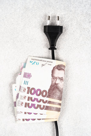 Plug and electic cable with Ukrainian currency hryvnyas banknotes on it. Increasing electricity prices in Ukraine. High electricity prices for household consumers. Power system crisisの写真素材