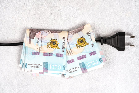 Electic cable and plug with Ukrainian banknotes hryvnyas on it. Ukrainian power system crisis. Increasing electricity prices in Ukraine. High electricity prices for household consumersの写真素材