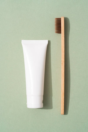 Vertical image of wooden bamboo toothbrush and tube with organic mineral toothpaste over green background. White plastic tube with toothpaste. Eco bath products, mockupの写真素材