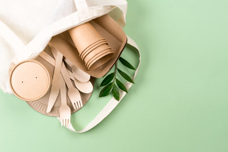 Paper utensils in white cotton bag over light green background with copy space. Kraft paper cups, food containers and bamboo cutlery set - paper tablewareの写真素材