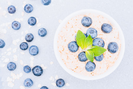 Healthy breakfast - oatmeal porridge served with blueberry and mint leaves in white bowl on concrete table background. Morning superfood porridge recipe. View aboveの写真素材
