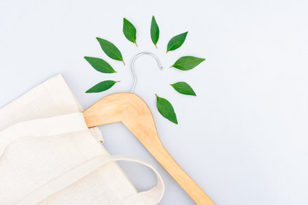 Wooden hangers, white cotton bag and green leaves over light gray background with copy space. Eco fashion. Green shopping and slow fashion conceptの写真素材