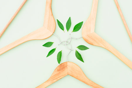 Wooden hangers with green leaves over light green background. Symbol of slow fashion. Reuse, recycling and upcycling clothes concept. Green shoppingの写真素材