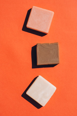 Handmade organic soap bars made with natural ingredients over red brown background. Making herbal soap at home. Flat lay style, mockup. Vertical compositionの写真素材