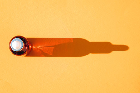 View above glass dropper bottle with face serum over orange background with bottle shape shadow. Beauty skin-care products, natural face beauty oil with vitamin Cの写真素材