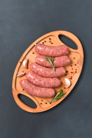 Raw sausages or bratwurst with seasonings on wooden plate over black stone table background ready to grill. Traditional pork sausages. Overhead view, vertical imageの写真素材