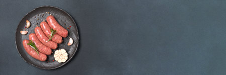 Long banner with raw sausages or bratwurst with seasonings on black plate over black stone background with copy space. Traditional pork sausages ready to cook. Overhead viewの写真素材