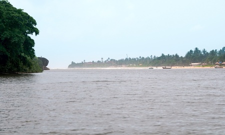 Tropical place where river meets with the ocean, people and boats on a shoreの写真素材